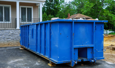 A blue large dumpster in front of a house.