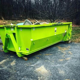 A green dumpster in the woods.